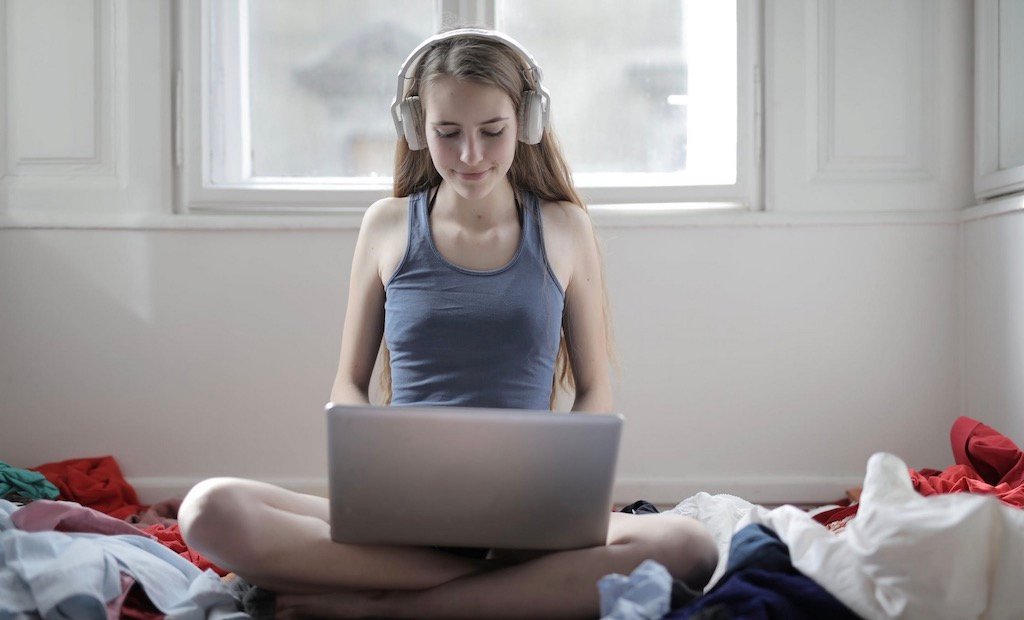 a lady sitting on her bed, with headphones and on her laptop showing operating systems for gaming